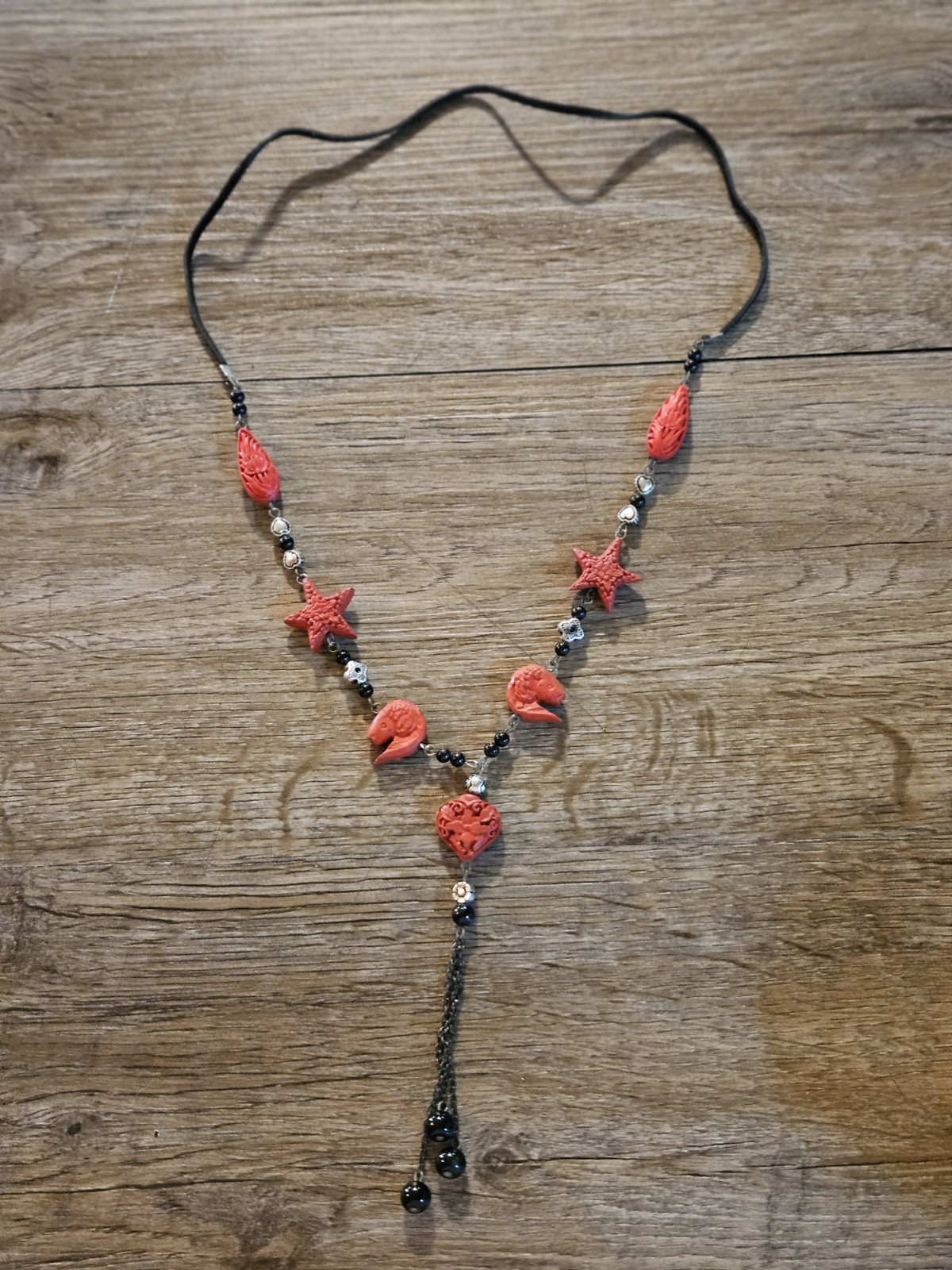 This red l and black lariat necklace features carved starfish and shrimp charms