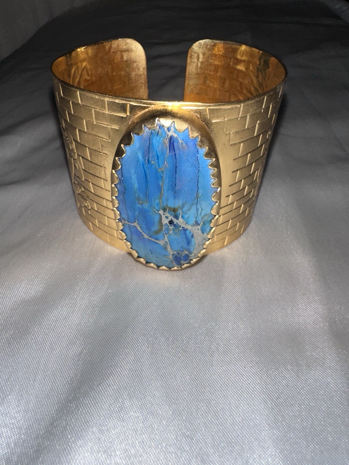 Gold-tone cuff bracelet with a bold blue stone and elegant engraved details.